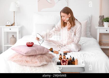 Young woman massaging face in bedroom Stock Photo