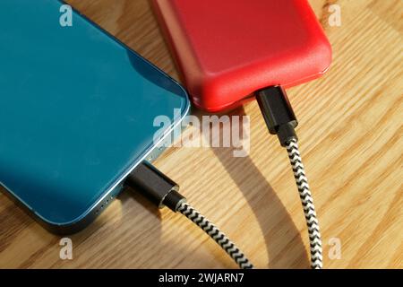 Back of red and blue two mobile phones connected to charging cables Stock Photo
