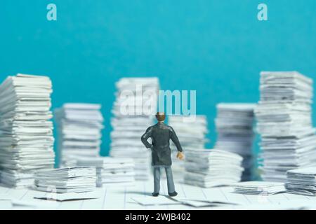 Miniature tiny people toy figure photography. File, task, work flow management plan concept. A businessman standing at a room full with pile of docume Stock Photo