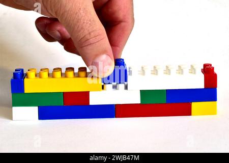 The man's hand inserts the missing piece into the construction made of Lego pieces. Stock Photo