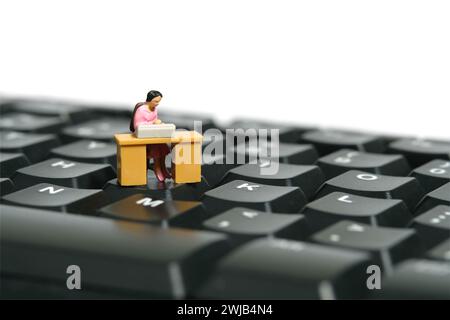 Miniature tiny people toy figure photography. A woman seat in the desk, working above keyboard. Isolated on a white background. Image photo Stock Photo