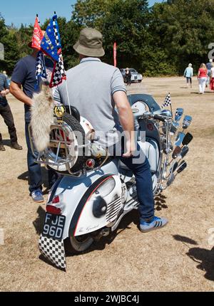 Man In Bucket Hat Sitting On A 1966 Vespa Douglas 124cc Scooter Motorcycle Adorned With Fox Tail, Mirrors, Flags in The Mod Style, Uk Stock Photo