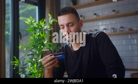 Man holding credit card and smartphone enters credit card number to online purchases. Male using instant easy mobile payments, making purchase in onli Stock Photo