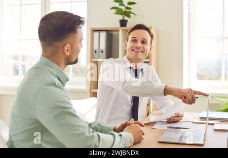 Two happy business men working in office sitting with laptop computer and smiling Stock Photo