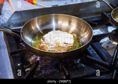 A piece of lamb leg is fried in oil in an iron pan. Stock Photo