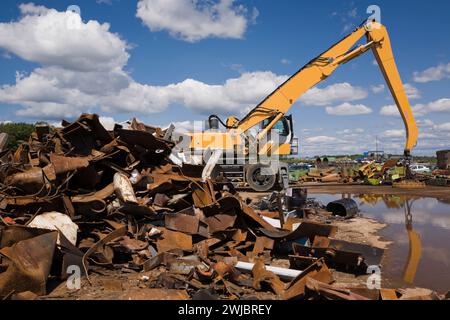 Assorted rusted steel, metal parts, pieces and crane loader with grappling arm at scrap metal recycling junkyard. Stock Photo