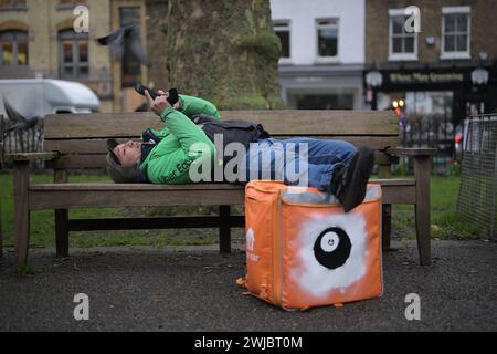 14th February 2024: An Uber Eats food courier takes a break between jobs in Islington Green, London. Deliveroo and Uber Eats couriers are striking tonight between five and ten o’clock to secure better working conditions and pay. Stock Photo