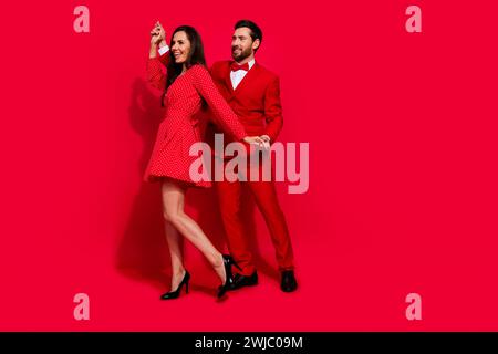 Full size photo of lovely young couple dance have fun disco valentine day dressed stylish elegant outfit isolated on red color background Stock Photo