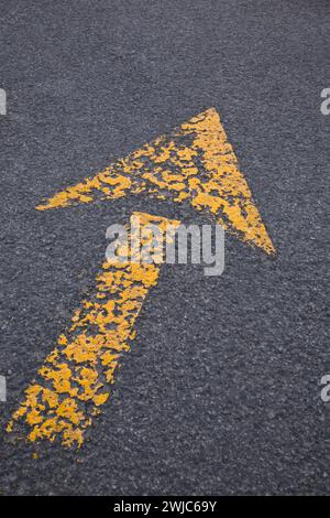Faded yellow painted traffic direction arrow on black asphalt pavement surface. Stock Photo
