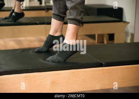 Young woman exercising on pilates reformer bed, feet close up