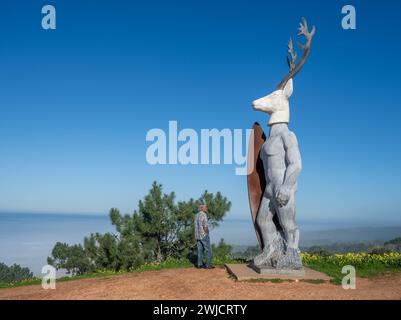 A man stands in front of a surfer statue with a deer head, Nazare, Portugal Stock Photo