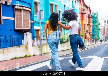 Rear view of two african american young friends walking along a colorful street Stock Photo