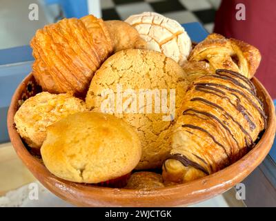 Close-up of a tempting assortment of Mexican sweet breads, featuring conchas, pastries, and muffins, presented in a traditional clay dish. Stock Photo