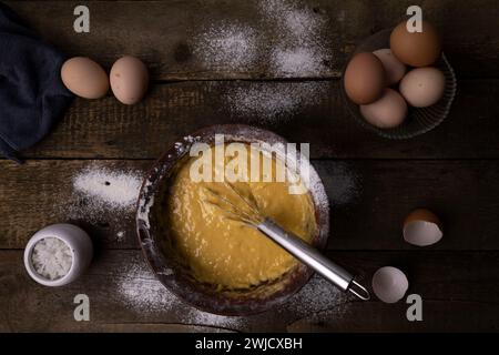 dough, broken chicken eggs, and kitchen items on a wooden table. Stock Photo