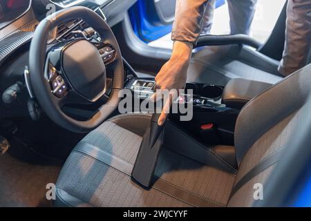 Car interior luxury service. Details of car cleaning male using professional steam vacuum for dirty car interior. Stock Photo