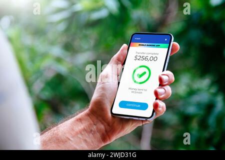 Man making money transfers online using apps to send and receive currency. Mobile phone with a financial application on screen. Money transfer concept Stock Photo