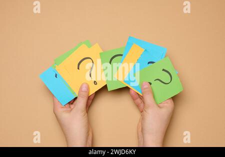 Female hands hold paper sheets with a drawn question mark on a beige background, searching for the answer and truth Stock Photo