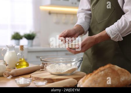 Making bread. Man putting dry yeast into bowl with flour at wooden table in kitchen, closeup Stock Photo