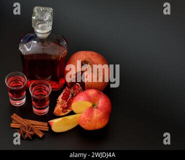 Apple pomegranate liqueur with cinnamon and anise, strong homemade alcohol in two glasses and a bottle on a black background. Close-up. Stock Photo