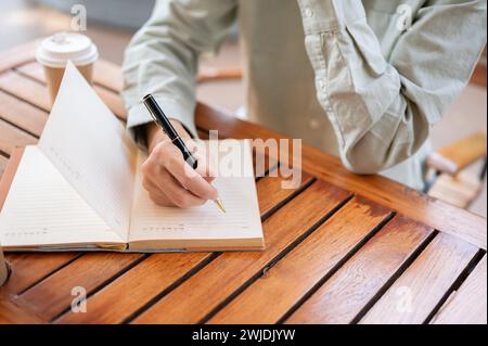 A close-up shot of a man writing in his notebook, jotting down ideas, or keeping a diary while sitting in a cafe. Stock Photo