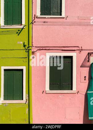 Front view of two old houses in Burano with painted walls, widows blinds, frames, and pipes Stock Photo