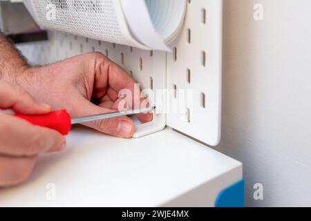Man screws pegboard on white work table with screwdriver Stock Photo
