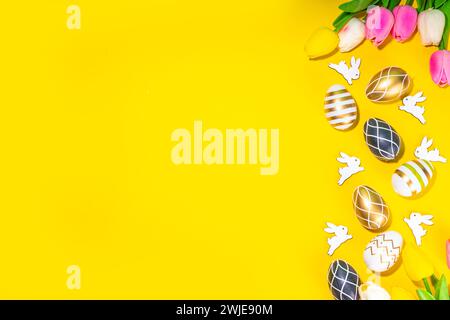 Bright Easter greeting card background. Trendy colored black, golden, stripe painted Easter eggs with white bunny rabbits decor, tulip flower on high- Stock Photo