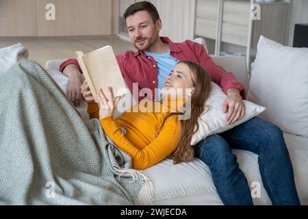 Happy loving family couple staying at home, relaxing, reading interesting novel, discussing on couch Stock Photo