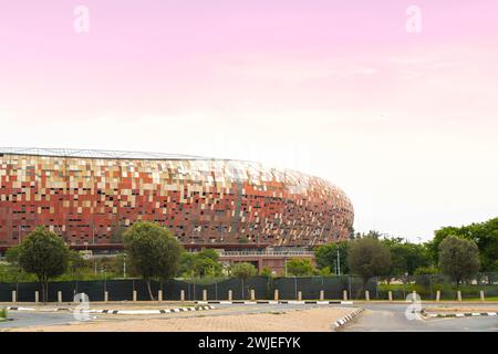 The iconic Soccer City Stadium in Johannesburg basks in the warm glow of a sunset, showcasing its distinctive mosaic facade against the evening sky. Stock Photo