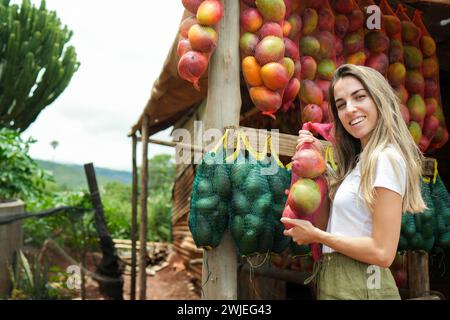 A happy woman is seen purchasing ripe mangoes from a colorful fruit stall along a countryside road in Africa, embodying the vibrancy of local markets. Stock Photo