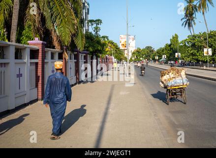 A muslim man wearing a traditional kanzu long tunic and kofia cap walks past the Azania Front Cathedral in Dar es Salaam, Tanzania. Stock Photo