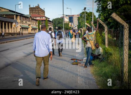 Commuters walk down Kivokoni Road past a street vendor towards Kigamboni Ferry Terminal in Dar es Salaam, Tanzania Stock Photo