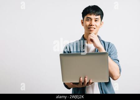 Portrait of a thoughtful man, holding a laptop, chin resting on his hand, engrossed in thinking Stock Photo