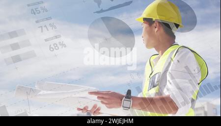 Asian male architect with plans atop a building, graphs in front Stock Photo