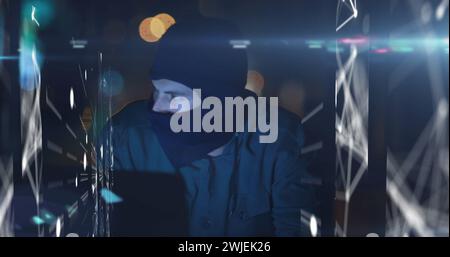 Image of digital interface with data processing over male hacker in balaclava using laptop Stock Photo