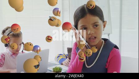 Image of digital interface with emoji icons floating over children using electronic devices Stock Photo