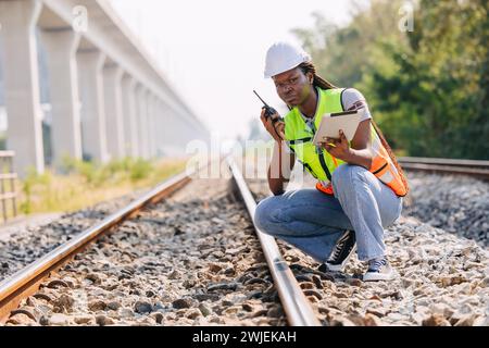 African black engineer women worker work checking service in train railway tracks construction site in transportation industry radio operate Stock Photo