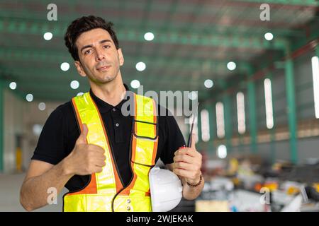 Engineer man hand like sign or factory worker wear safety helmet in warehouse site indoor Showing thumbs up happy smile.Good working finished job done Stock Photo
