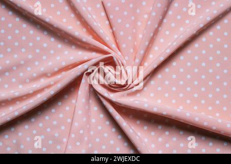 Texture of twisted pink fabric with white dots. Fabric is twisted into a bundle in the center. Stock Photo