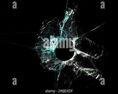 Broken glass texture with bullet hole and green cracks on black background. Macro close up. Stock Photo
