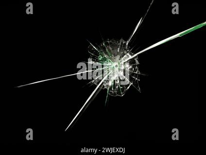 Bullet hole in glass with long intersecting cracks and green reflections on black background. Macro. Close up. Stock Photo