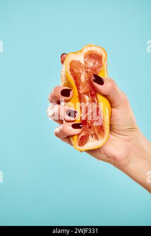 unknown woman with nail polish squeezing gourmet fresh grapefruit in her hand on blue background Stock Photo