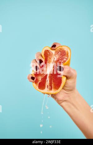 unknown young female model with nail polish squeezing fresh juicy grapefruit on blue backdrop Stock Photo