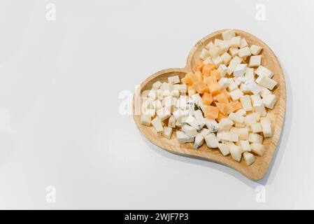A variety of cheese on a wooden plate in the shape of a heart.  Stock Photo