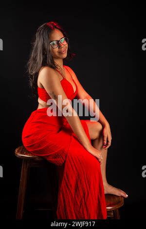 Salvador, bahia, Brazil - December 09, 2023: Portrait of beautiful young woman wearing glasses and in red dress sitting posing for photo. Isolated on Stock Photo