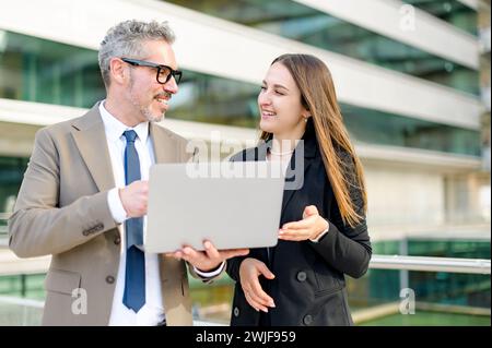 A senior businessman with a grey hair shares ideas and strategy with a young female colleague over a laptop, reflecting teamwork and mentorship in a modern corporate setting Stock Photo