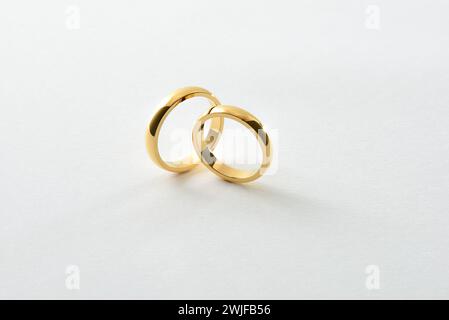 Detail of engagement gold rings standing perpendicular to each other isolated on white textured background. Elevated view. Stock Photo