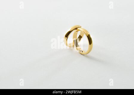 Detail of engagement gold rings leaning on each other isolated on white textured background. Elevated view. Stock Photo