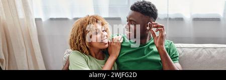 happy african american man in hearing aid device sitting on couch with girlfriend, banner Stock Photo