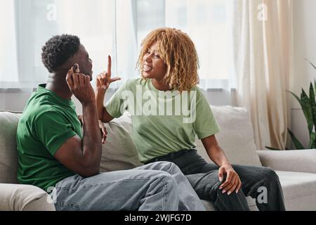 African American couple communicating using a sign language on couch, black man in hearing aid Stock Photo